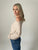 Woman wearing a beige long-sleeve top and blue jeans against a plain background