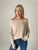 Woman wearing a beige off-shoulder sweater and blue jeans against a plain background